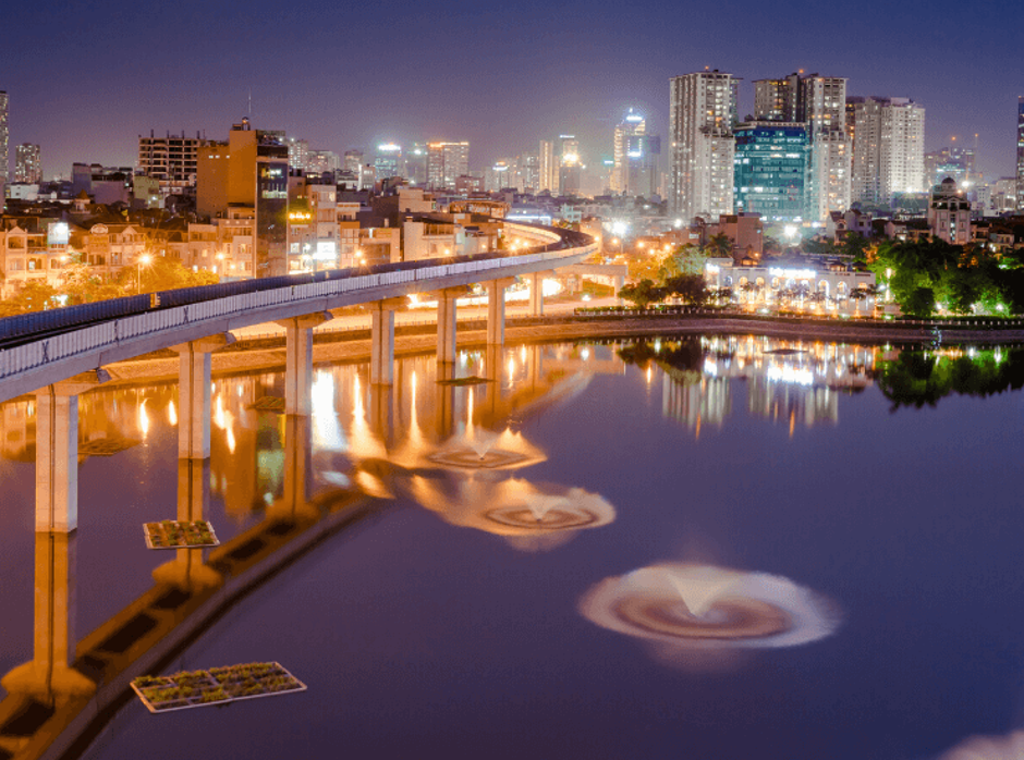 City skyline at night with an illuminated elevated railway and reflections on the water